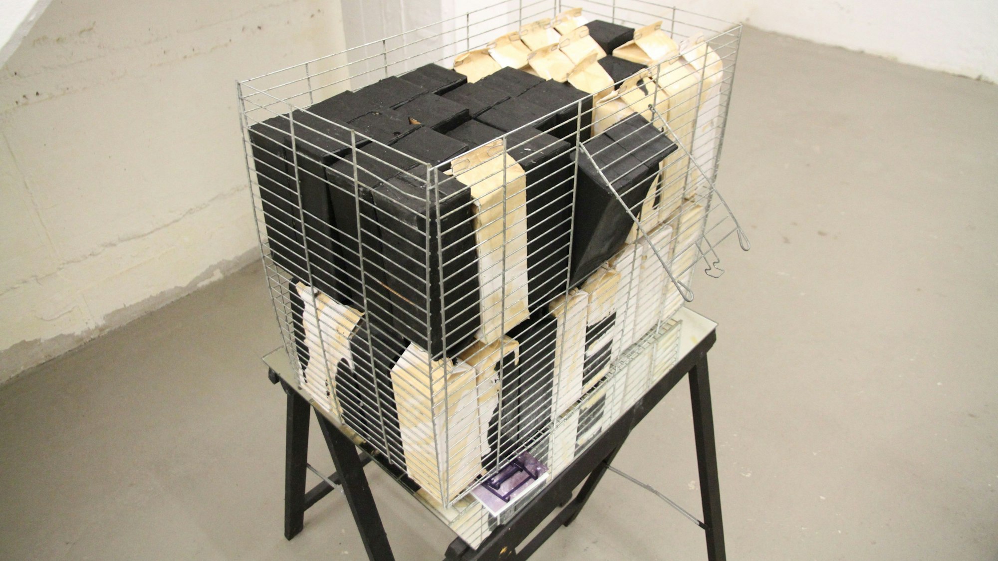 Ein Käfig birgt weiße und schwarze Milchkartons