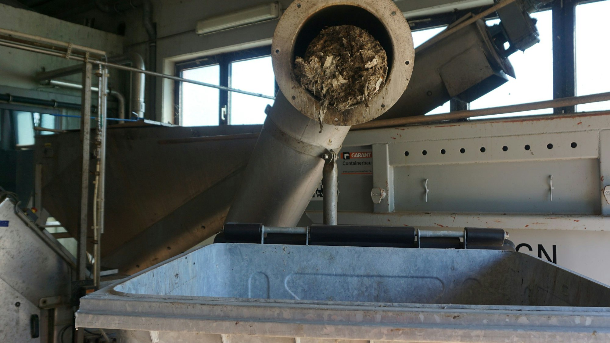 Das Bild zeigt ein geöffnetes Rohr. Abfall presst sich heraus. Darunter steht ein Container.