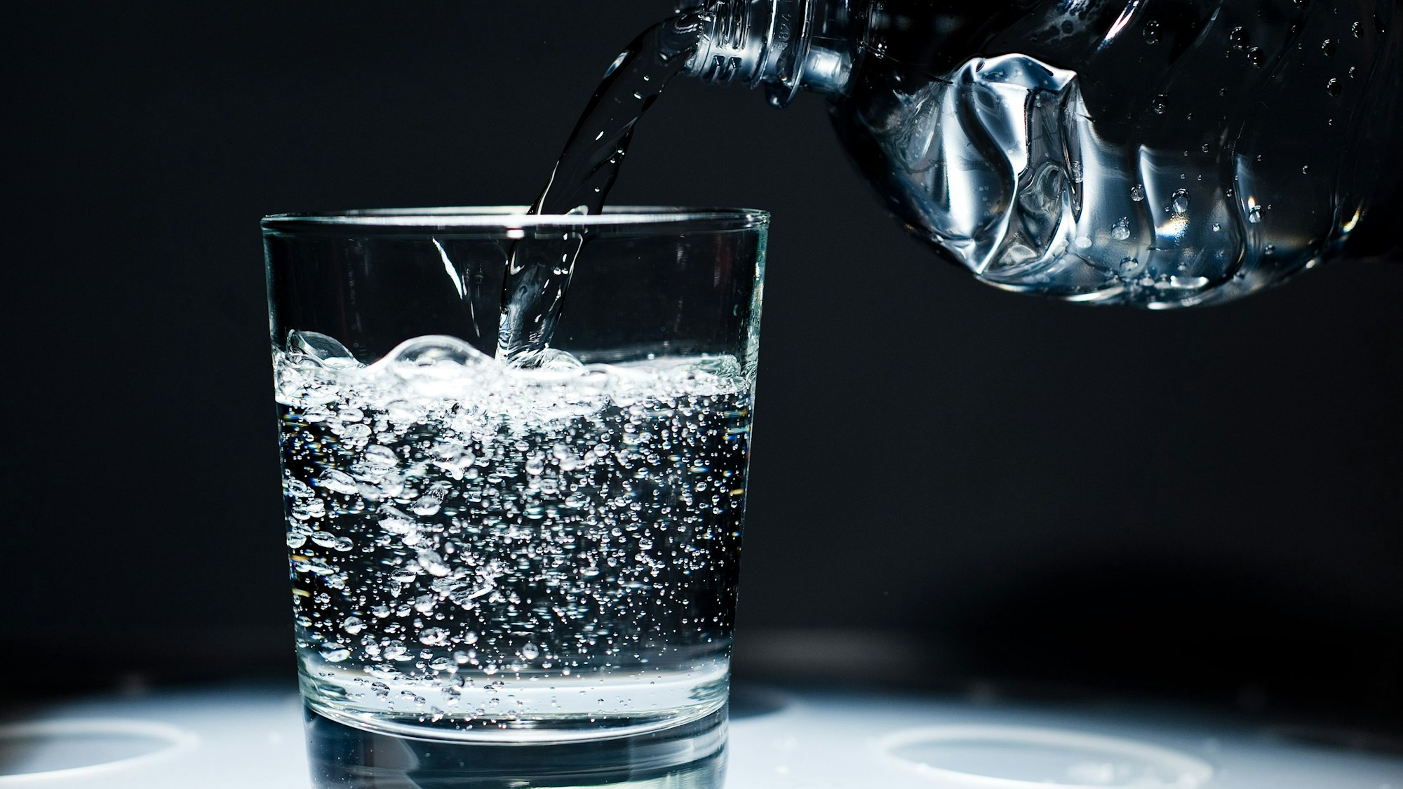 Sprudelwasser wird aus einer Flasche in ein Glas geschüttet.