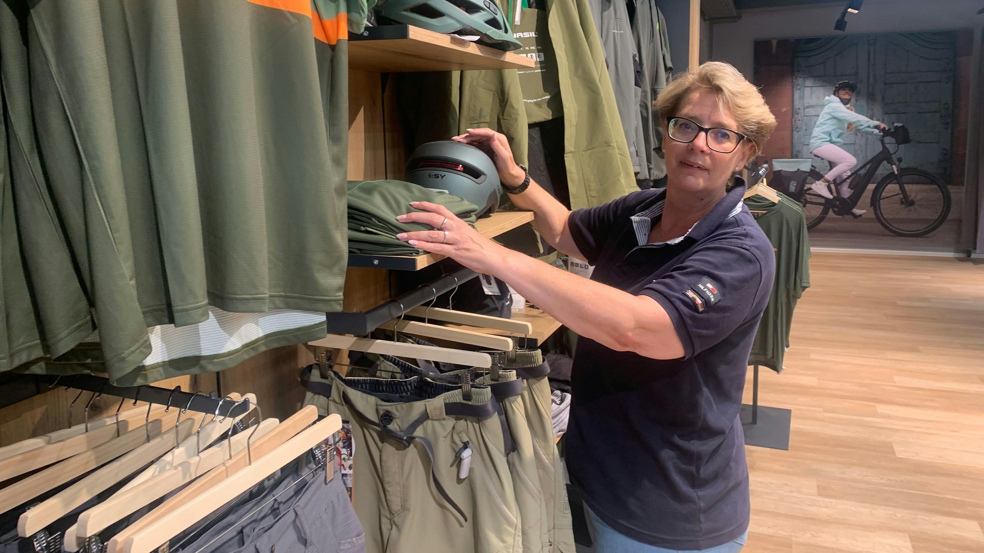 Textil-Abteilungsleiterin Sylke Burmeister rückt Hemden zurecht, die auf Bügeln an einer Stange hängen.