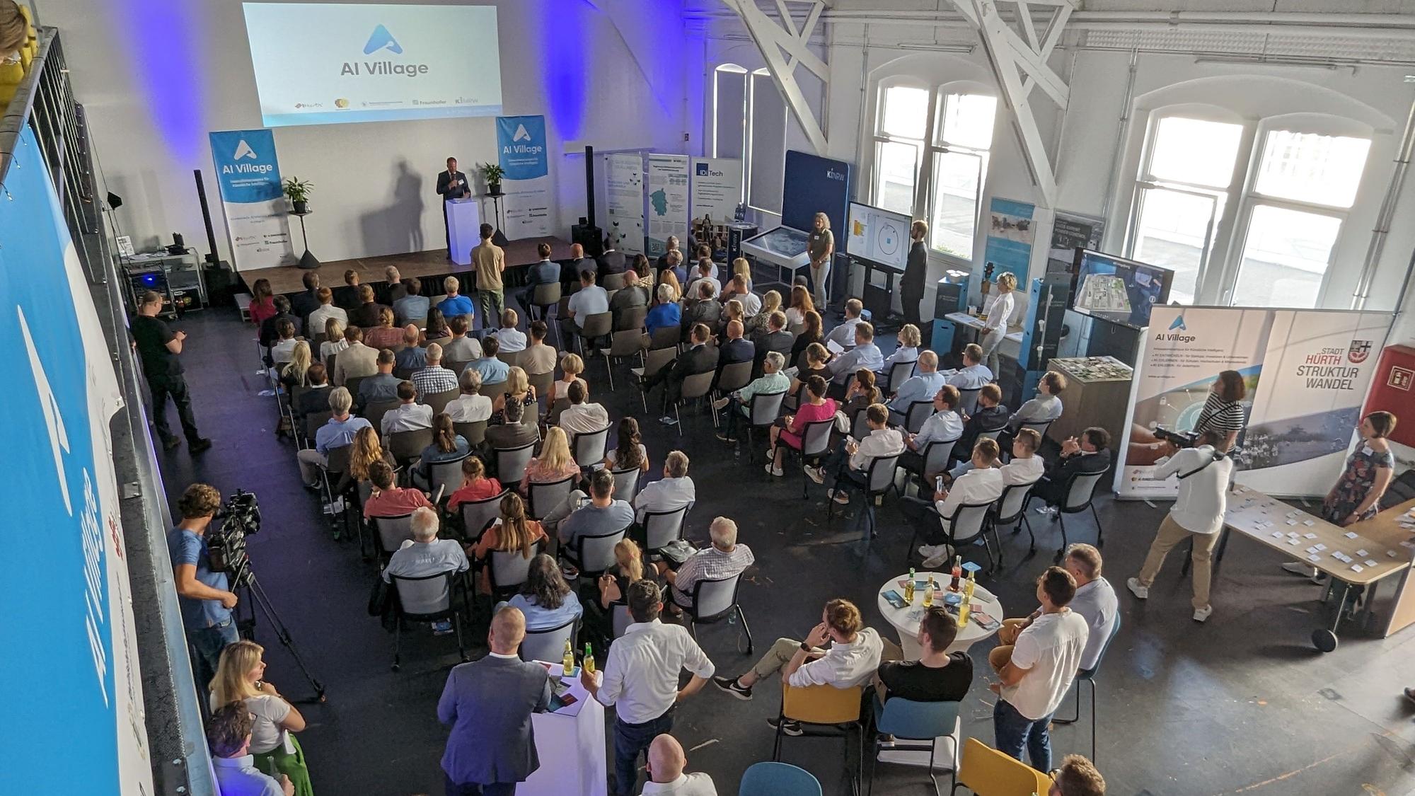 Volle Sitzreihen und Stellwände in einem Saal.