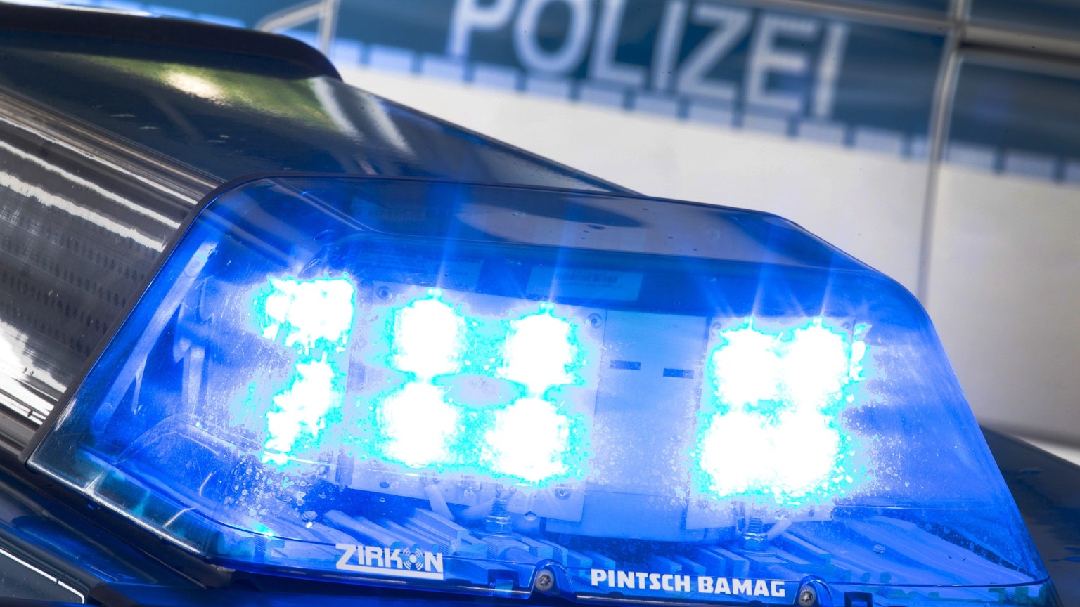 Ein Blaulicht leuchtet auf dem Dach eines Polizeiwagens. Im Hintergrund steht ein weiterer Streifenwagen.