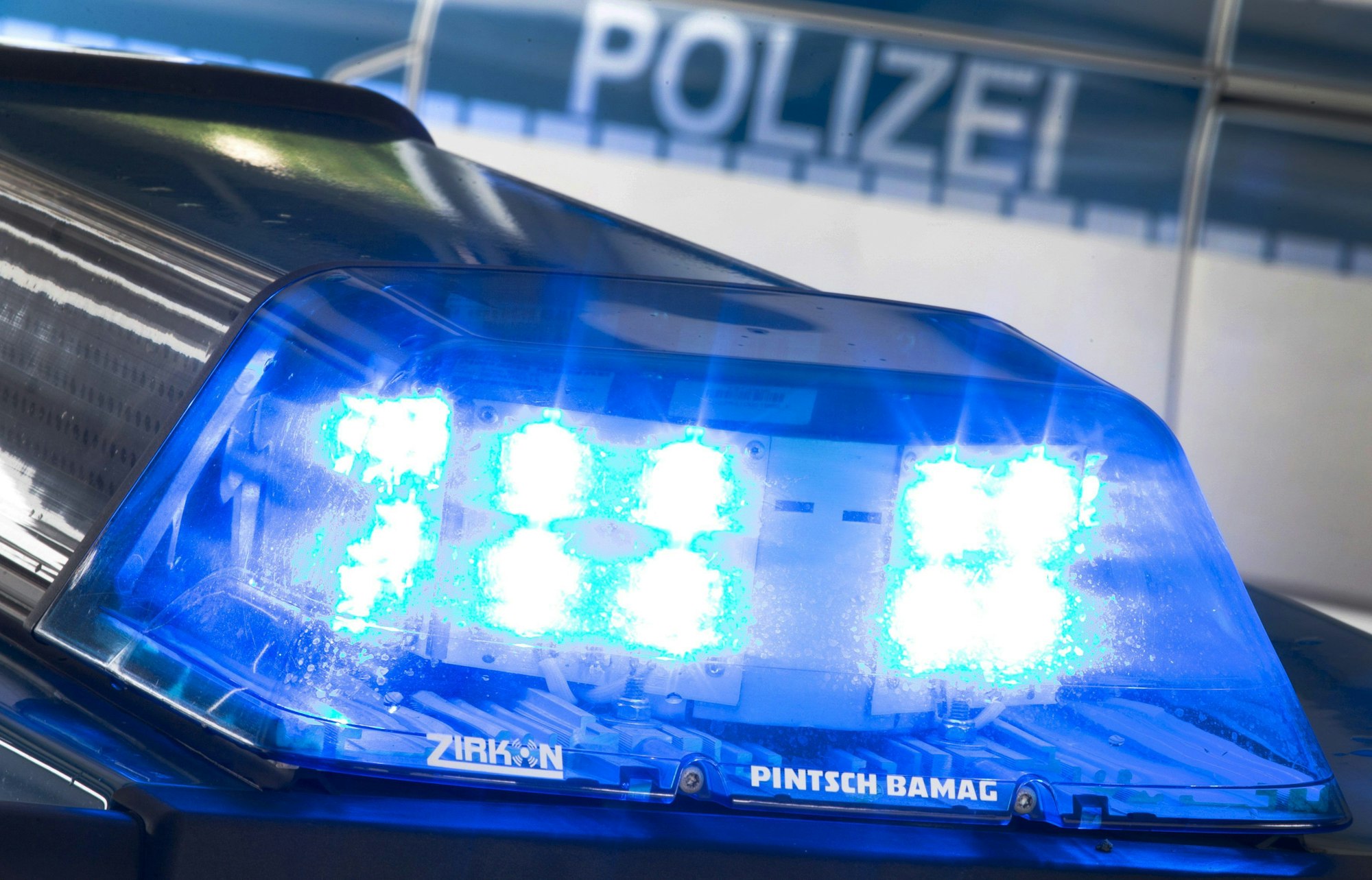 Ein Blaulicht leuchtet auf dem Dach eines Polizeiwagens. Im Hintergrund steht ein weiterer Streifenwagen.