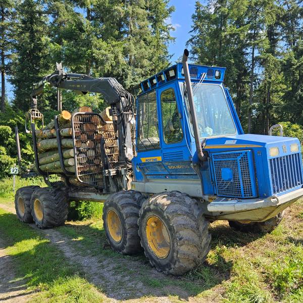 Ein blaue Rückemaschine transportiert Stämme auf der Ladefläche.