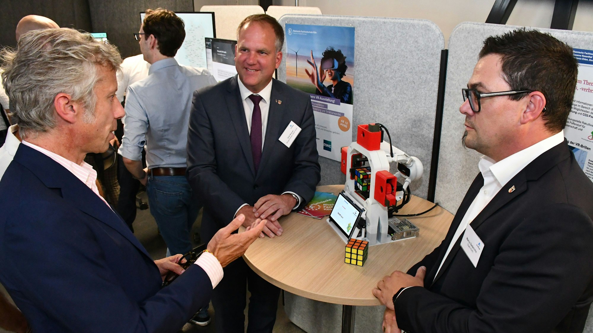 Drei Männer um einen Stehtisch, auf dem ein Roboter aufgebaut ist und ein Zauberwürfel liegt.