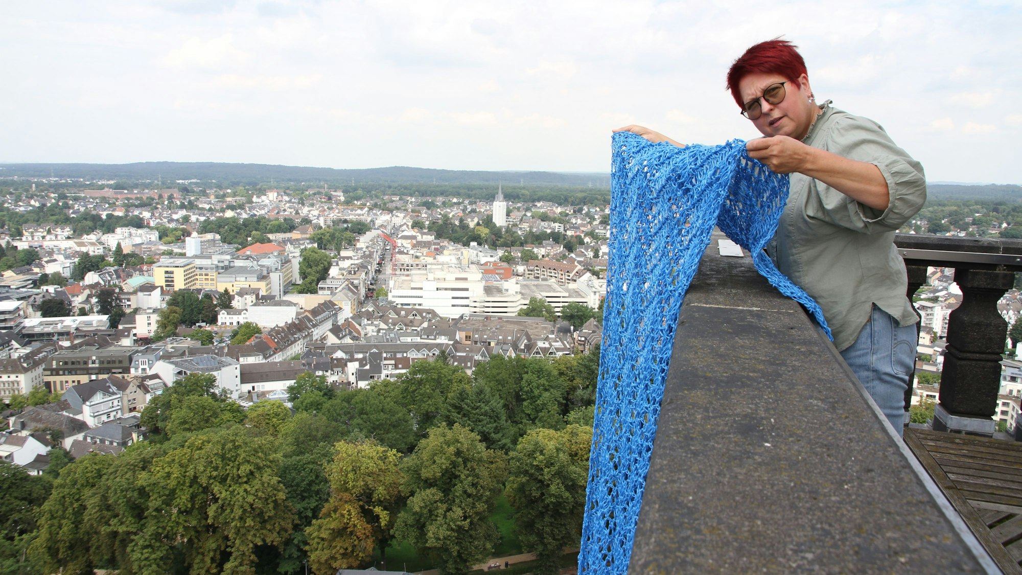 Künstlerin Katharina Krenkel legt ein blaues Banner aus gehäkelter Kunststoffschnur über die Brüstung der Aufsichtsplattform auf dem Siegburger Abteiturm