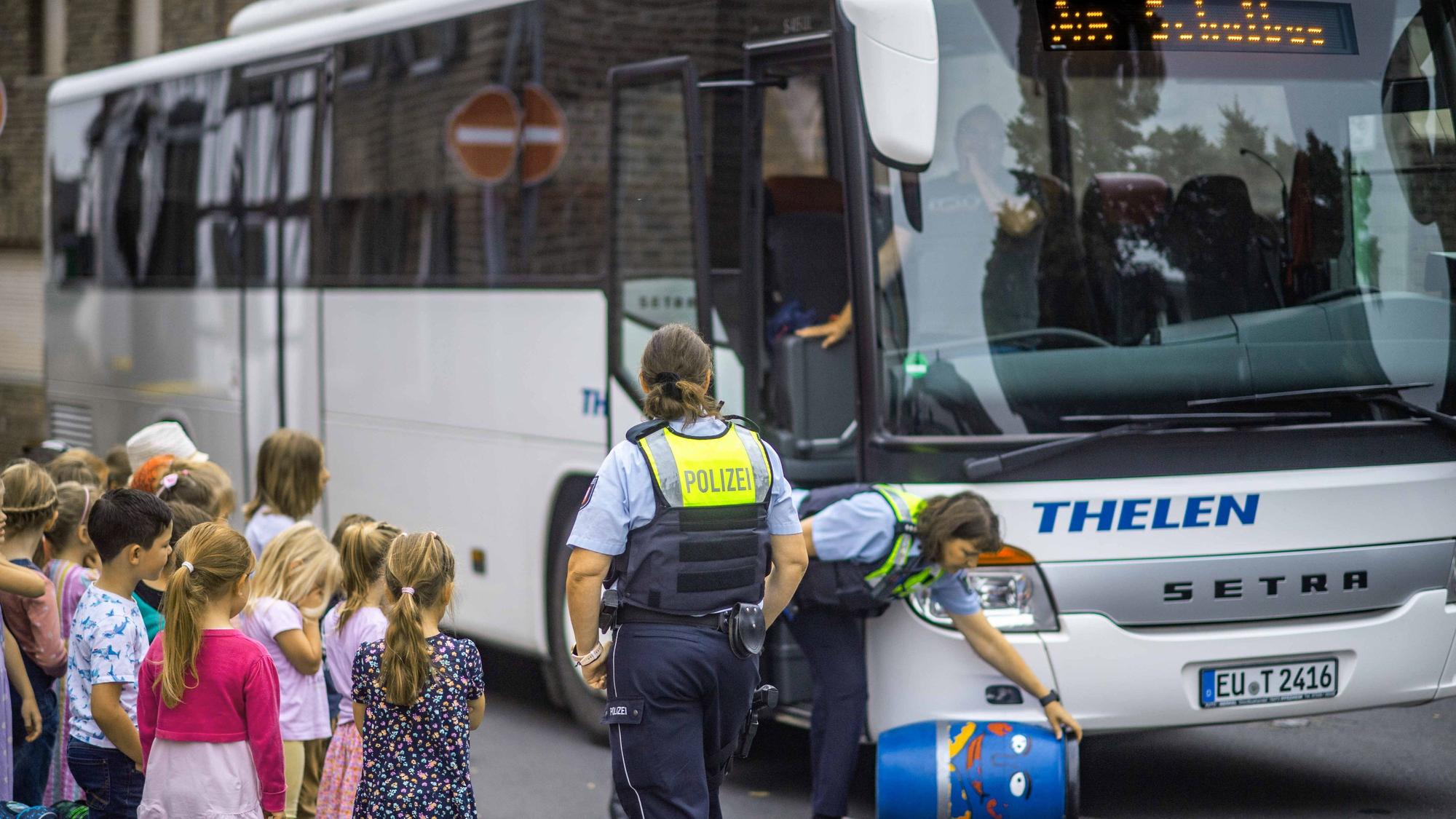 Das Bild zeigt zwei Polizistinnen, wie sie mit Grundschülern an einem Bus das richtige Verhalten lernen.