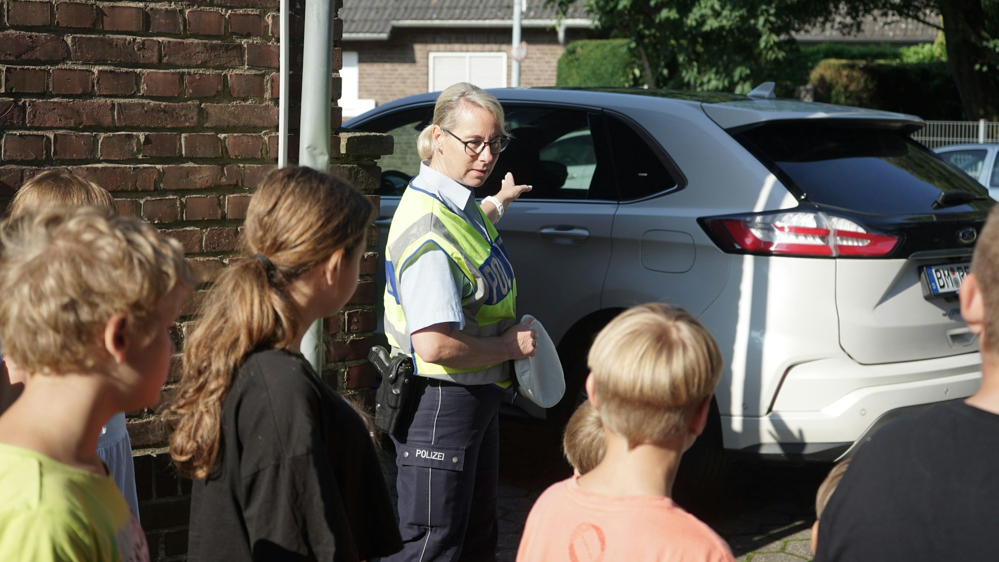 Polizistin Claudia Färber zeigt auf ein Auto in einer Einfahrt. Kinder hören ihr zu.
