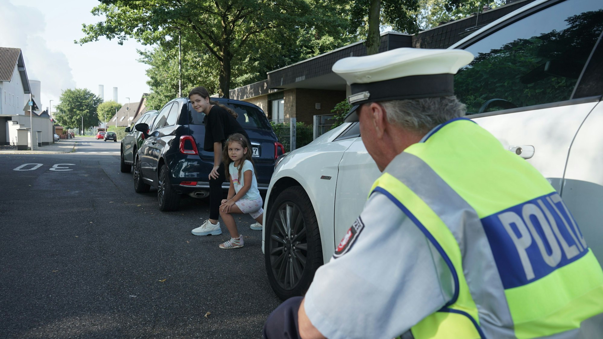 Das Bild zeigt den knieenden Polizisten Hans-Dieter Ehlert und zwei Kinder, die zwischen zwei Autos auf die Straße gucken.