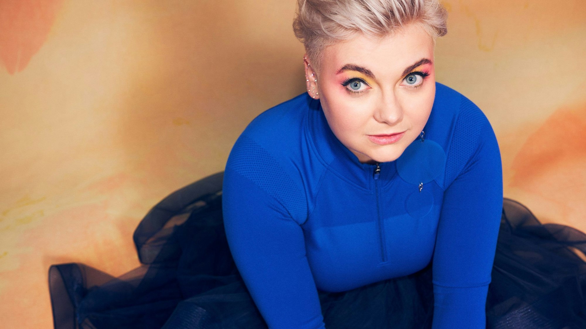 Sängerin Ela sitz in einem blauen Kleid auf dem Boden.