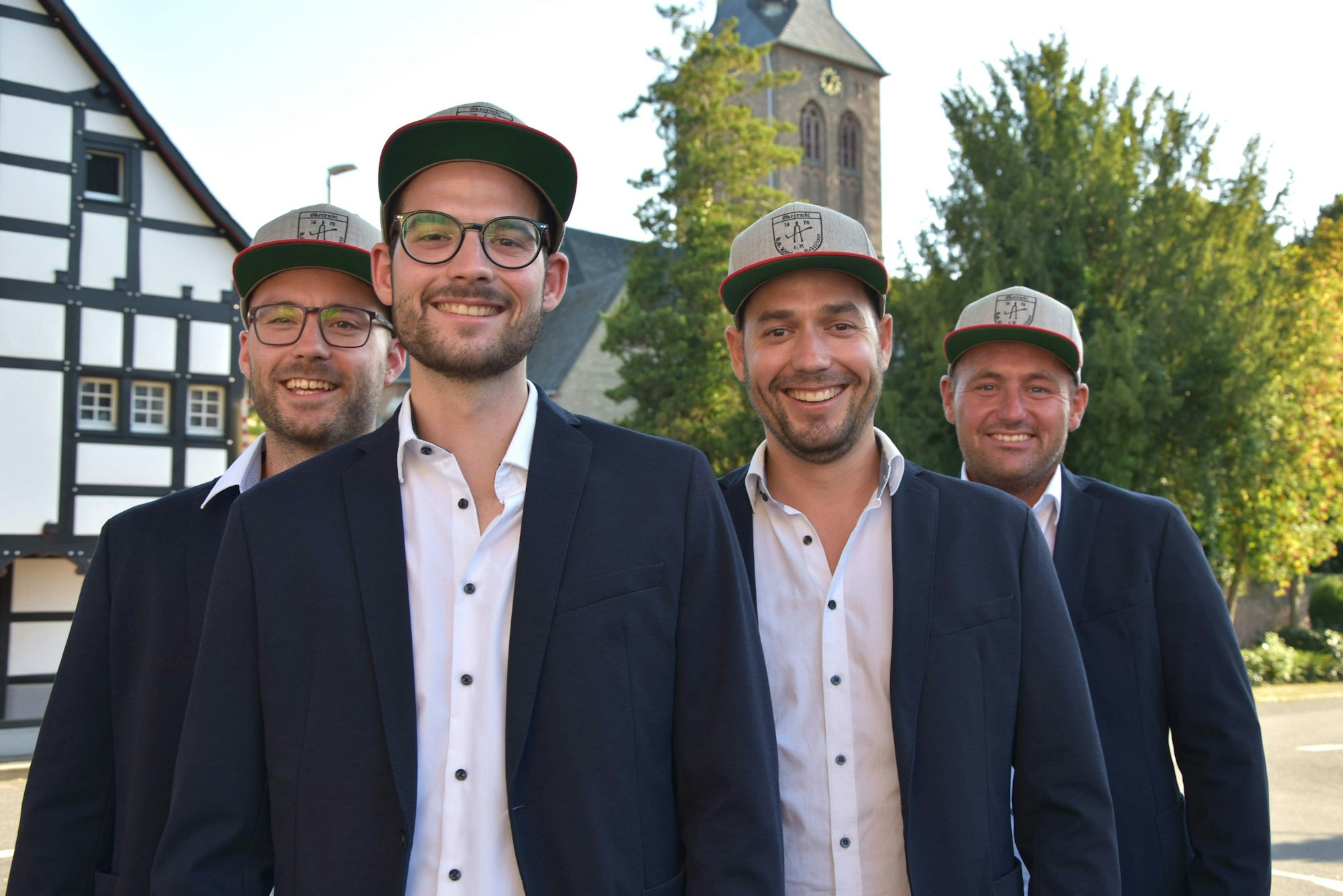 Vier junge Männer mit Kappen stehen vor einer Kirche.
