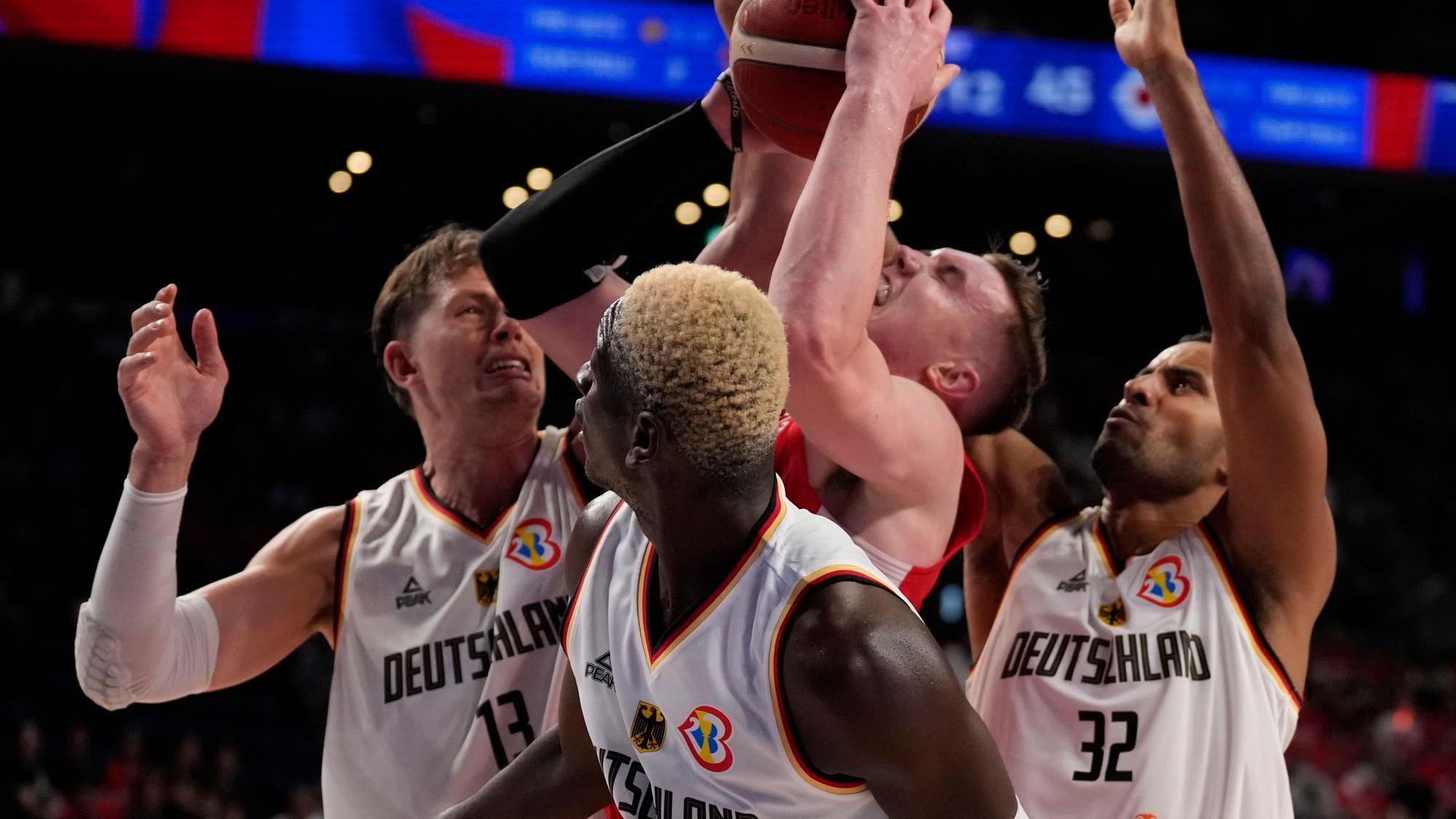 Japans Center Josh Hawkinson (24), Mitte, wird von Deutschlands Stürmer Moritz Wagner (13), von links, Guard Isaac Bonga (0) und Deutschlands Stürmer Johannes Thiemann (32) in der zweiten Halbzeit des Basketball-Weltmeisterschaftsspiels der Gruppe E zwischen Deutschland und Japan in Okinawa, Südjapan, am Freitag, 25. August 2023, unter Druck gesetzt.