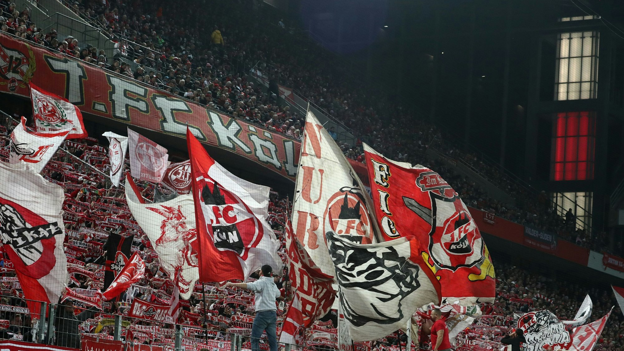 Auf einer Tribüne halten Fußball-Fans rot-weiße Schals hoch und schwenken Fahnen.