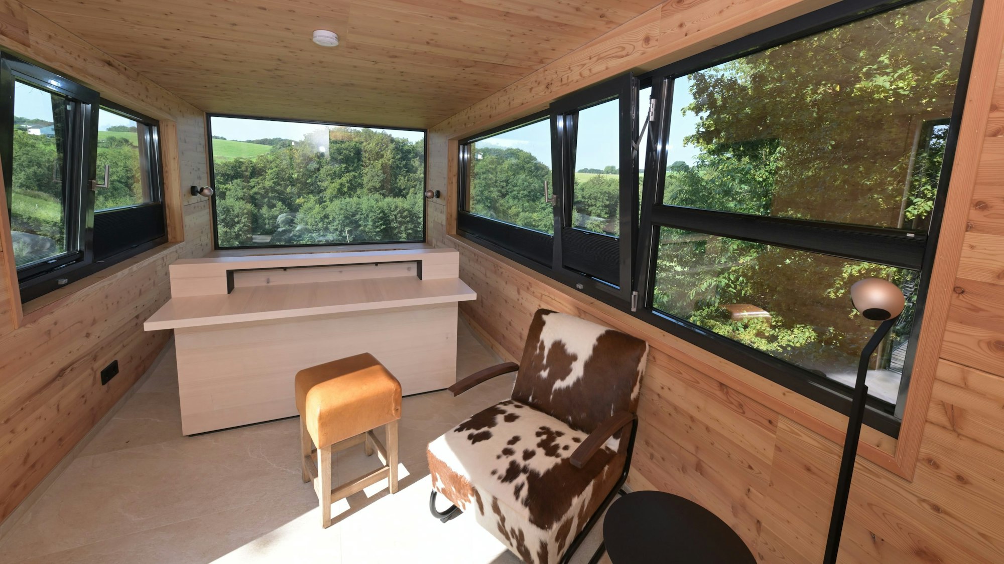 Ein Zimmer mit zwei Sesseln und großen Panoramascheiben, durch die man Wiesen und Bäume sieht.