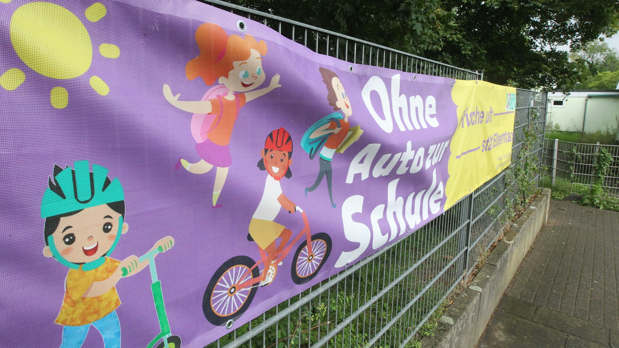 Ein Banner an einem Zaun wirbt für einen Schulweg ohne Auto.