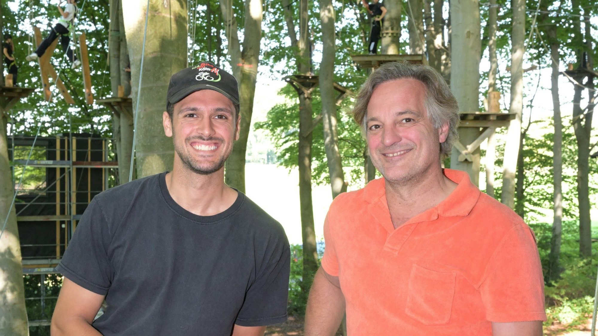 Vater und Sohn vor Bäumen eines Kletterwaldes.