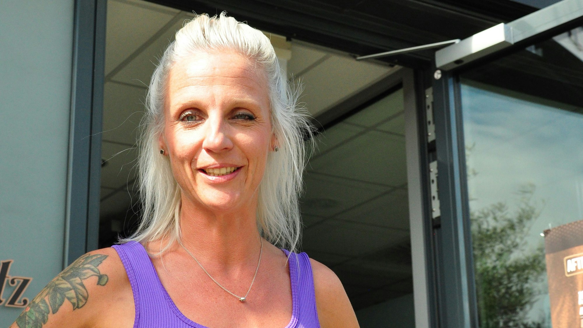 Eine Frau mit hellen Haaren und lilafarbenem Top steht in einer Tür.