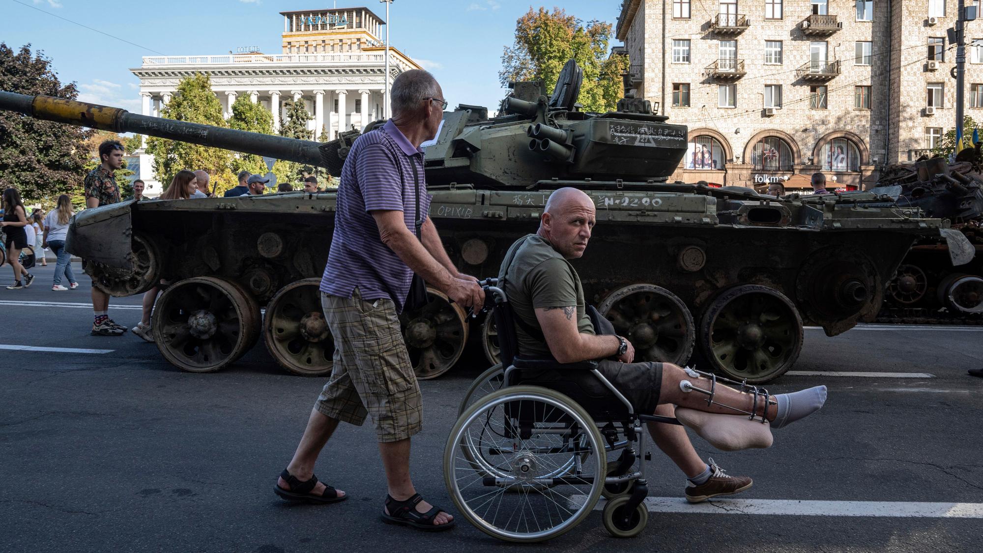 Ein verwundeter ukrainischer Soldat im Rollstuhl vor einem zerstörten russischen Panzer, der anlässlich des ukrainischen Unabhängigkeitstages am 24. August in Kiew ausgestellt wurde.