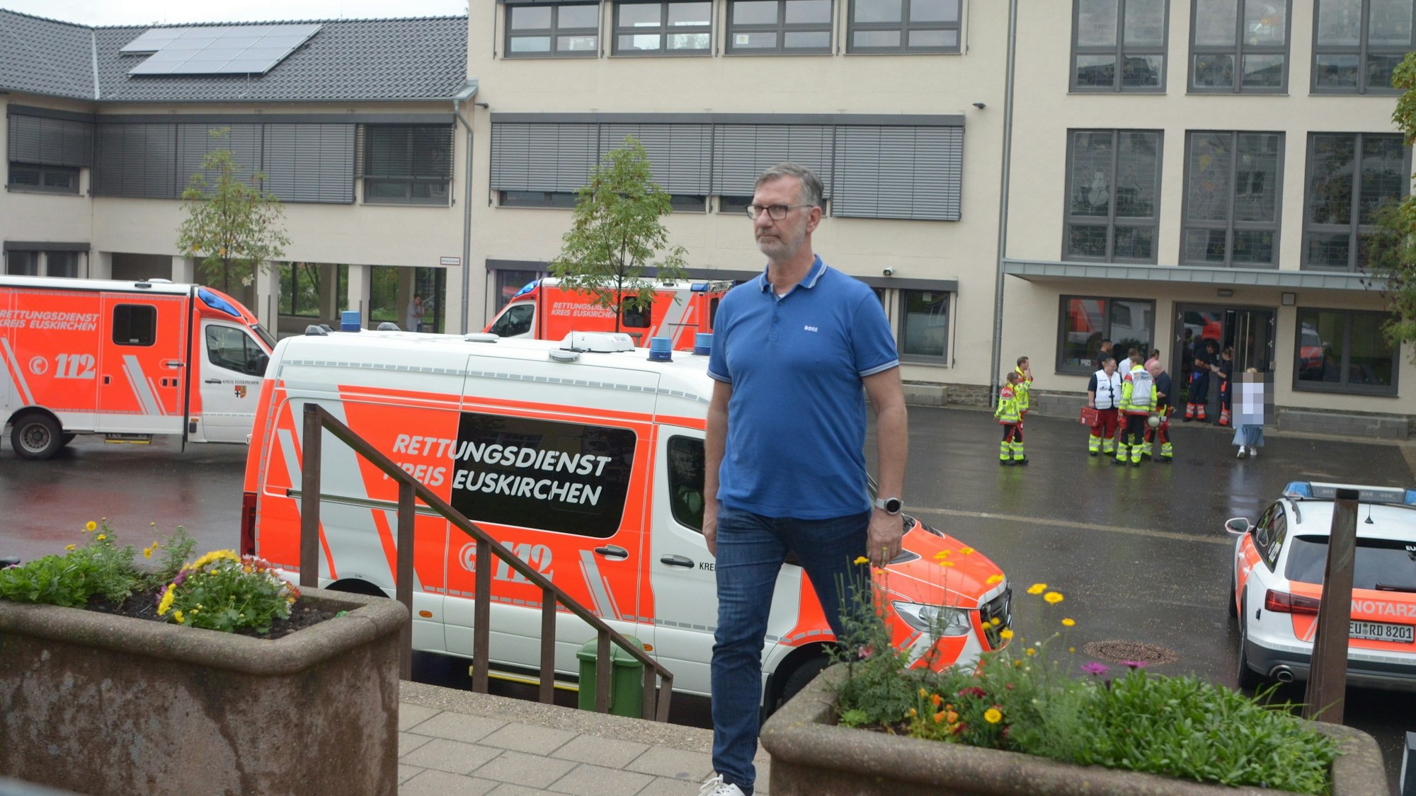 Der Leiter der Euskirchener Gesamtschule, Thomas Müller, geht eine Treppe hinauf. Im Hintergrund sind zahlreiche Rettungswagen zu sehen, die nach der TikTok-Challenge an der Schule im Einsatz waren.