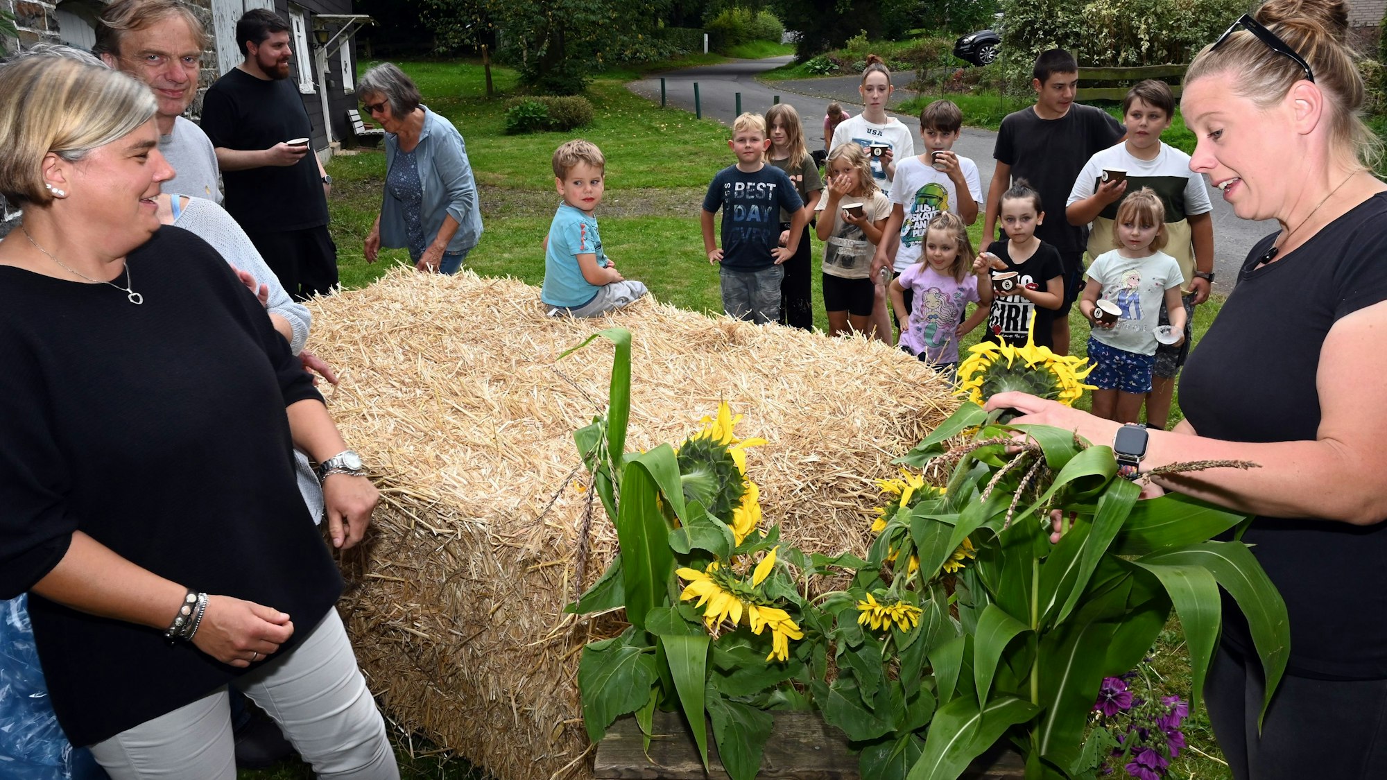 In der Waldbröler Ortschaft Happach laufen die Vorbereitungen für den „Autofreien Sonntag“ längst auf Hochtouren. Monia Schmelzer (r.) von der Dorfgemeinschaft sortiert Sonnenblumen für ein Gebinde, die anderen stapeln Strohballen zu Sitzmöbeln. Die Erwachsenen sind von Kindern umringt.