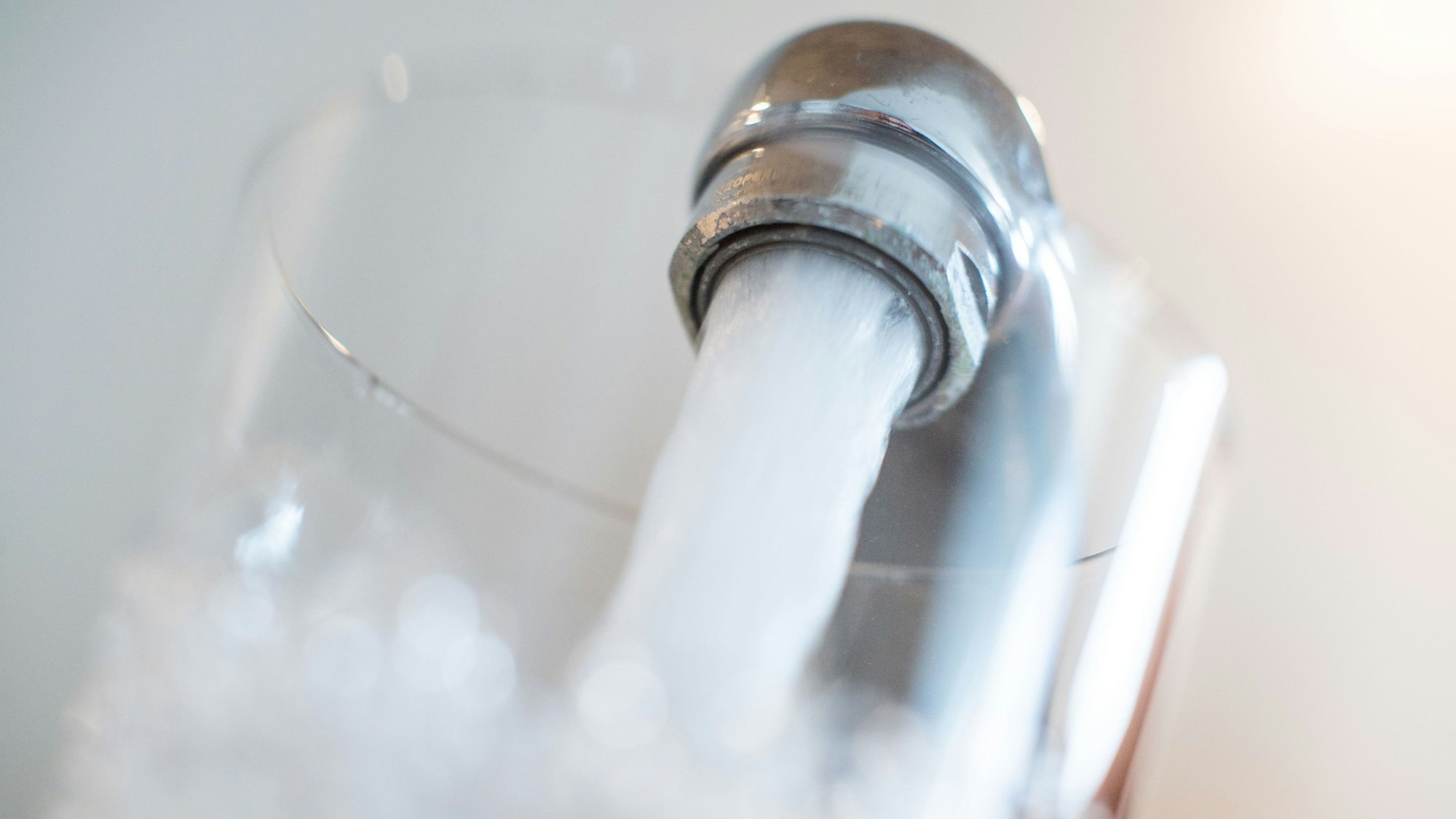 Ein Glas wird unter den Wasserhahn gehalten.