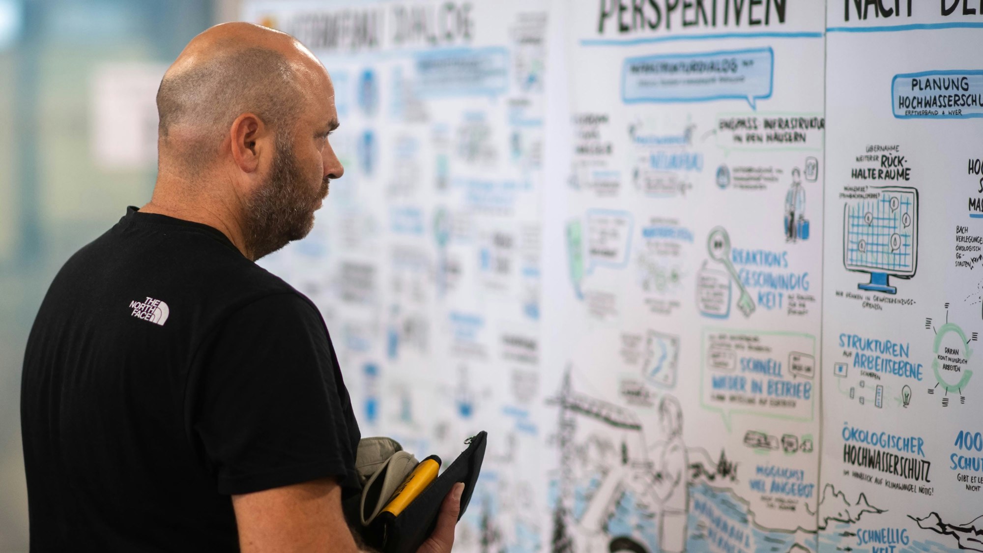 Das Bild zeigt einen Mann, der die handgezeichnete Karte des ersten Wiederaufbaudialogs betrachtet.