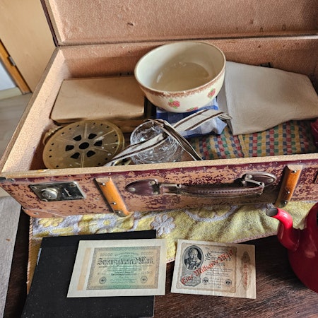 Ein Koffer mit Tüchern, einer Kaffeekanne und alten Geldscheinen ist zu sehen.