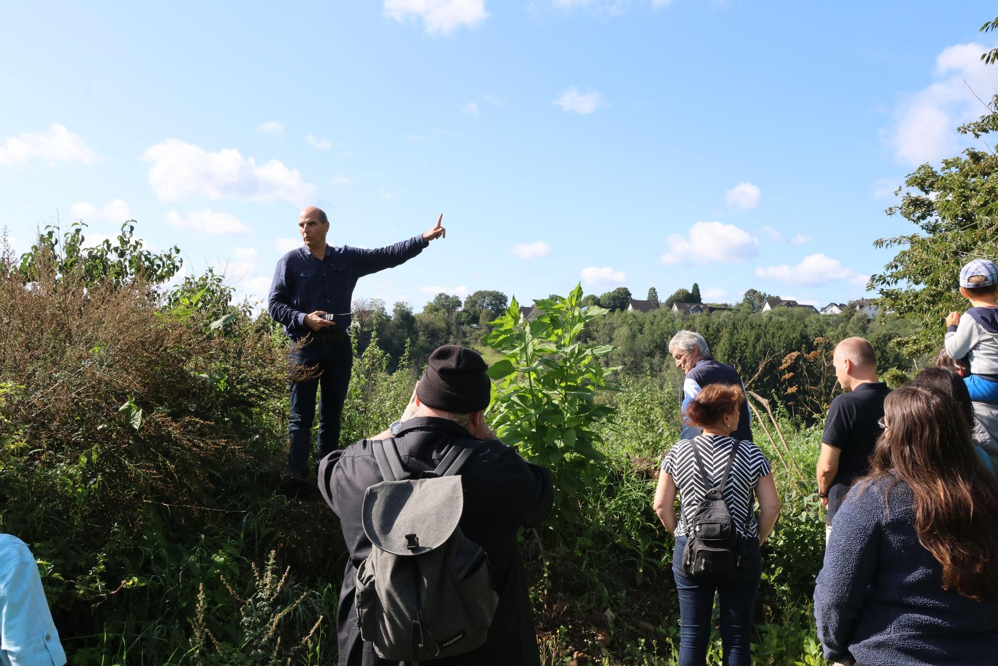 Die Gruppe der Interessierten ist auf einer Anhöhe oberhalb des Hallenbades „Monte Mare“ in Reichshof-Eckenhagen angekommen. Dort nimmt Investor Markus Lüdorf – mit dem Finger zeigend – Stellung zum geplanten Parkplatz für die Sommerrodelbahn.