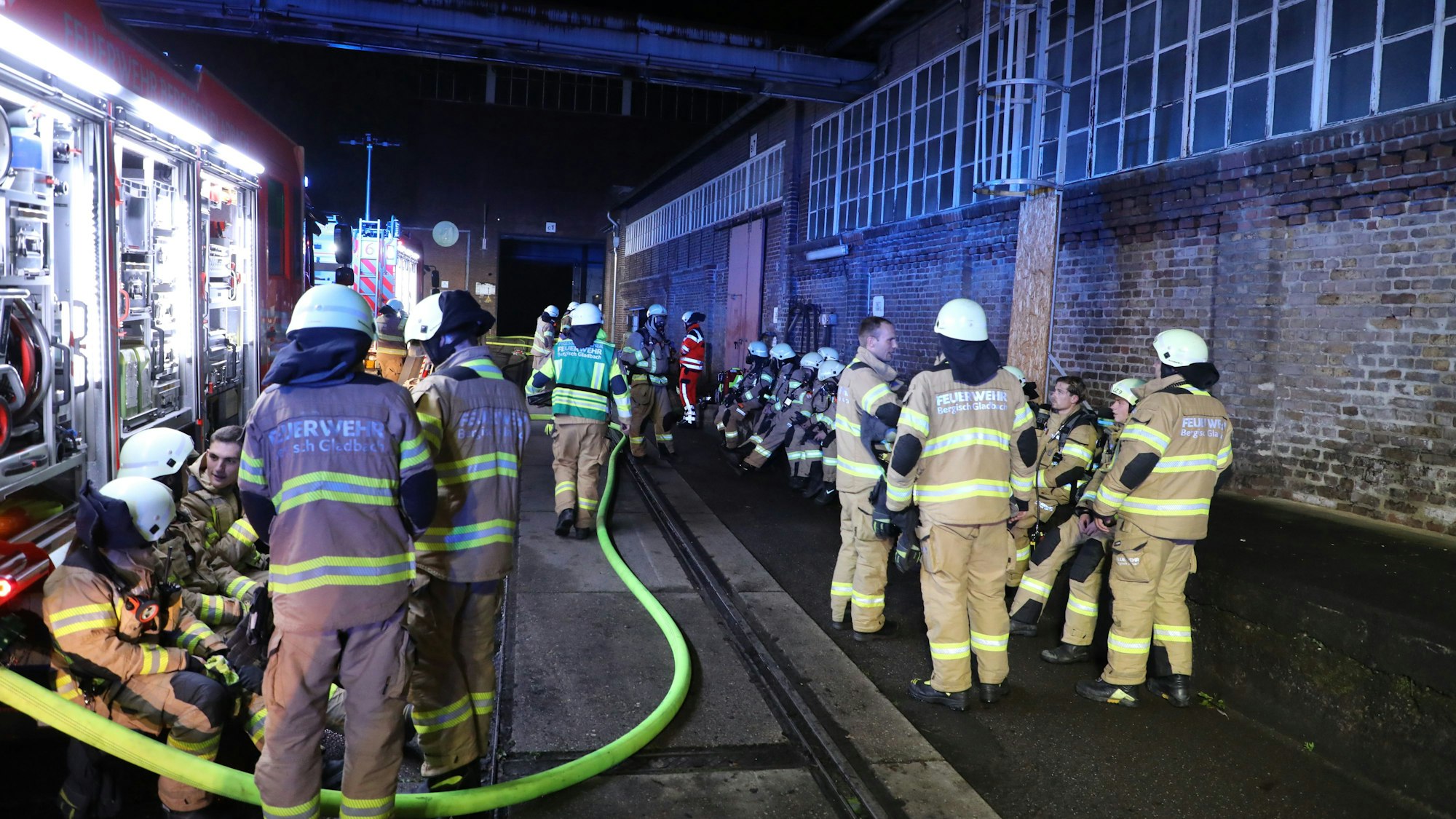 Feuerwehrleute arbeiten zwischen Feuerwehrfahrzeugen und einer Halle auf dem Zanders-Gelände.