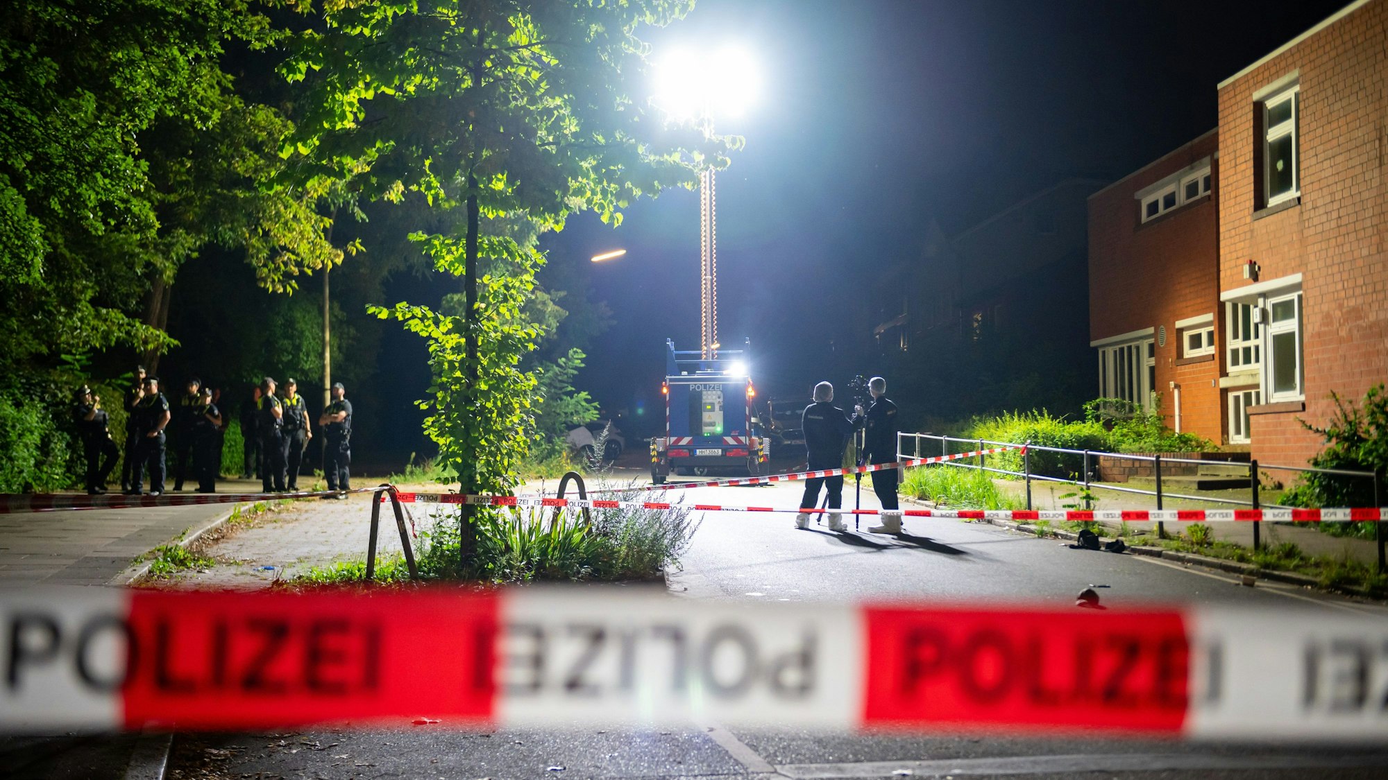 Ein Lichtmast erhellt den abgesperrten Tatort während Kriminaltechniker mit einem 3D-Scanner arbeiten und weitere Polizeibeamte ermitteln.