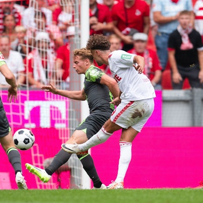 26.08.2023, Nordrhein-Westfalen, Köln: Fußball: Bundesliga, 1. FC Köln - VfL Wolfsburg, 2. Spieltag, RheinEnergieStadion. Kölns Luca Waldschmidt (r) trifft zur 1:0 Führung. Daneben stehen Wolfsburgs Yannick Gerhardt (l) und Nicolas Cozza. Foto: Marius Becker/dpa - WICHTIGER HINWEIS: Gemäß den Vorgaben der DFL Deutsche Fußball Liga bzw. des DFB Deutscher Fußball-Bund ist es untersagt, in dem Stadion und/oder vom Spiel angefertigte Fotoaufnahmen in Form von Sequenzbildern und/oder videoähnlichen Fotostrecken zu verwerten bzw. verwerten zu lassen. +++ dpa-Bildfunk +++