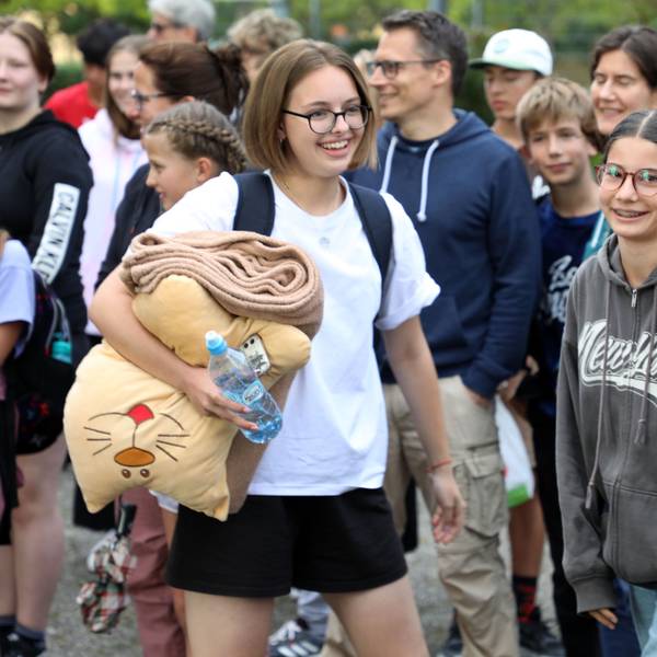 Schülerinnen und Schüler, Lehrerinnen und Lehrer und Eltern und andere Menschen stehen mit Fahnen von Ukraine, Deutschland, Butscha und Bergisch Gladbach auf dem Schulhof der Integrierten Gesamtschule Paffrath und jubeln.