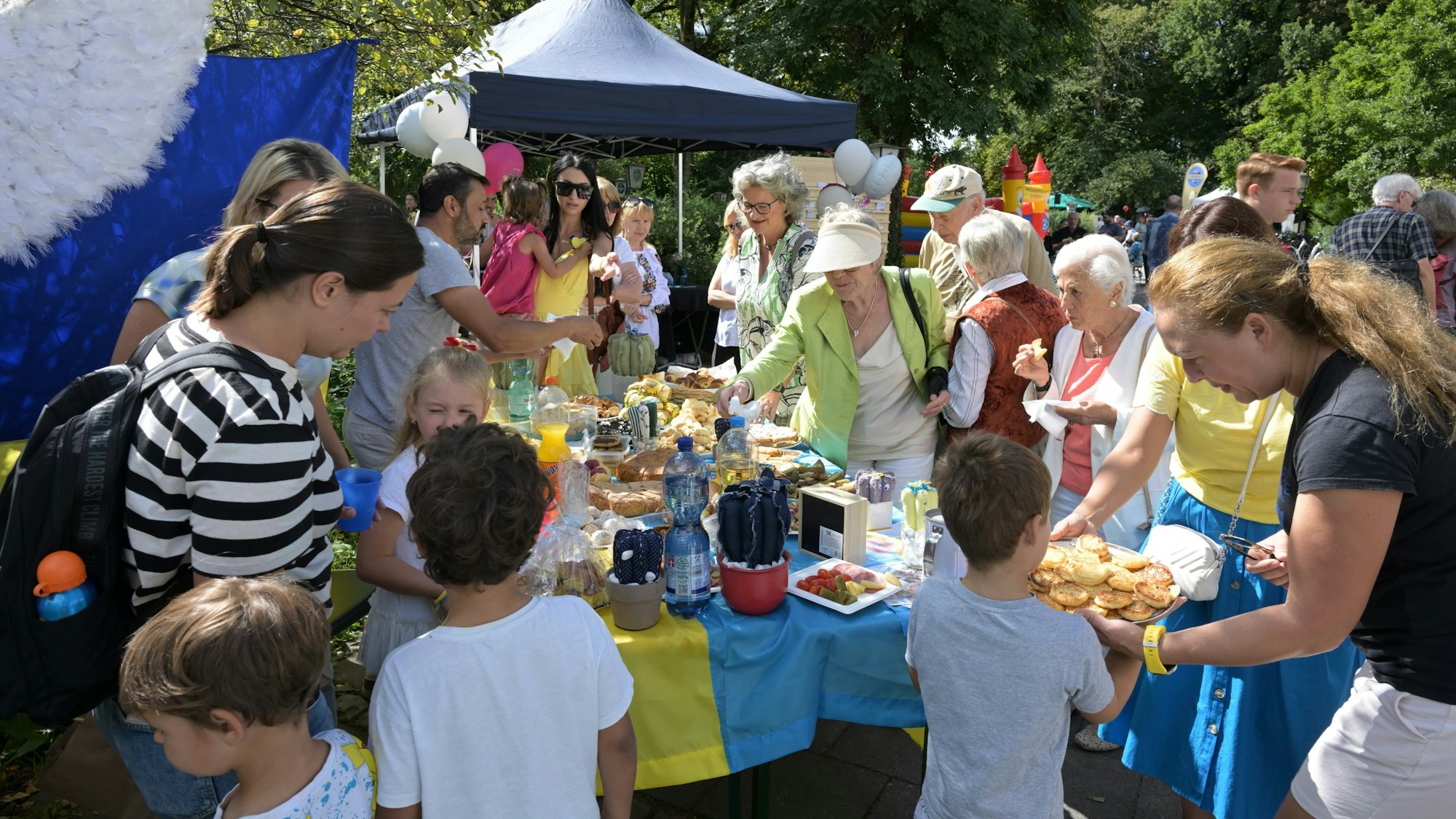 Kinder und Erwachsene umlagern einen bunten Stand mit Getränken und Fingerfood.