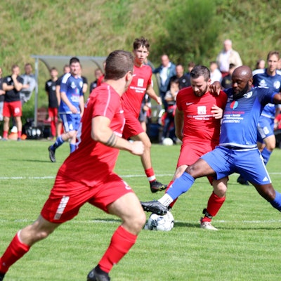 Zwei Spieler im Zweikampf um den Ball. Im Hintergrund sind die Zuschauer zu sehen.