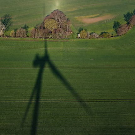 Das Foto zeigt den Schatten einer Windenergieanlage auf einem Feld.