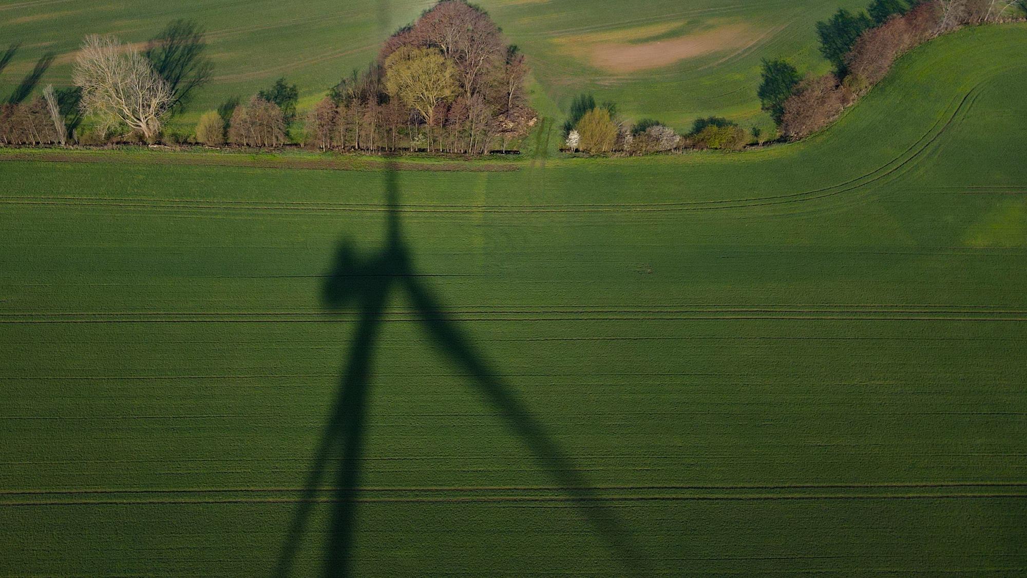 Das Foto zeigt den Schatten einer Windenergieanlage auf einem Feld.