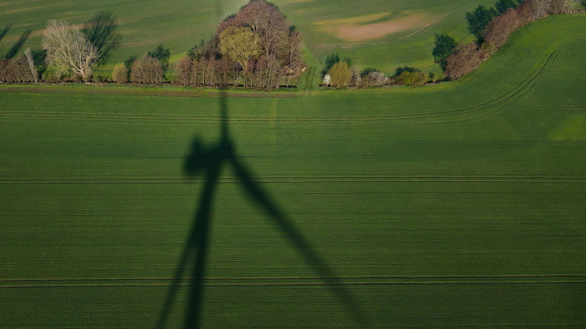 Das Foto zeigt den Schatten einer Windenergieanlage auf einem Feld.