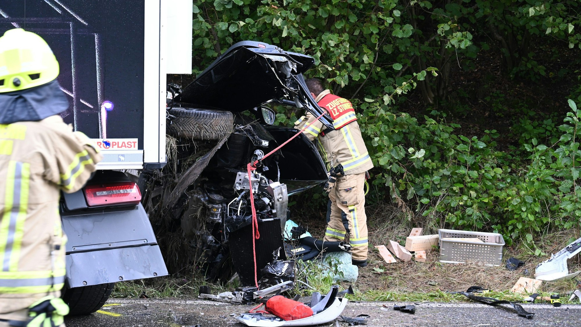 Ein Feuerwehrmann steht nach dem tödlichen Unfall in Pulheim vor dem völlig zerstörten Autowrack.