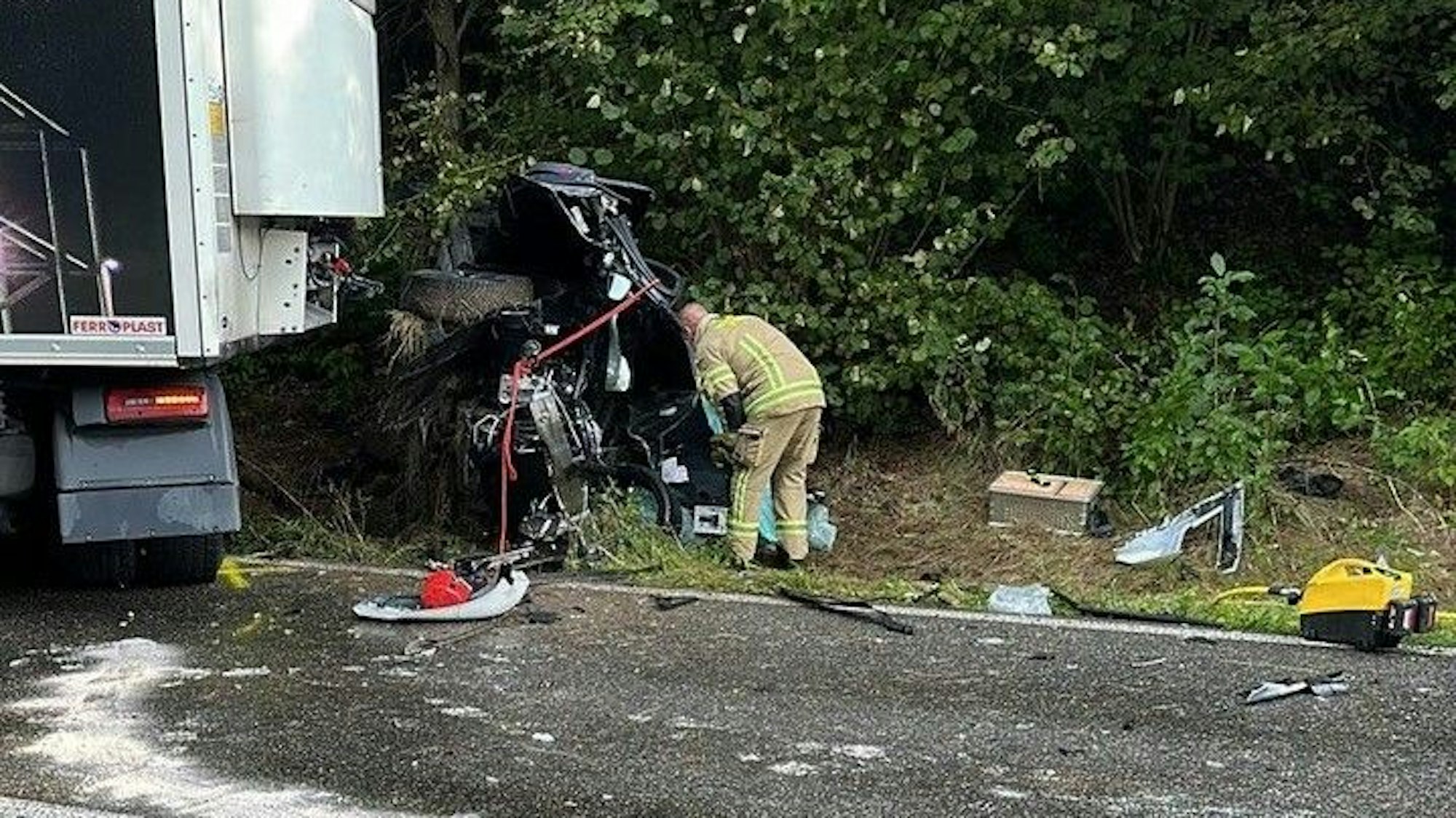 Ein Feuerwehrmann steht nach dem tödlichen Unfall in Pulheim vor dem völlig zerstörten Autowrack.