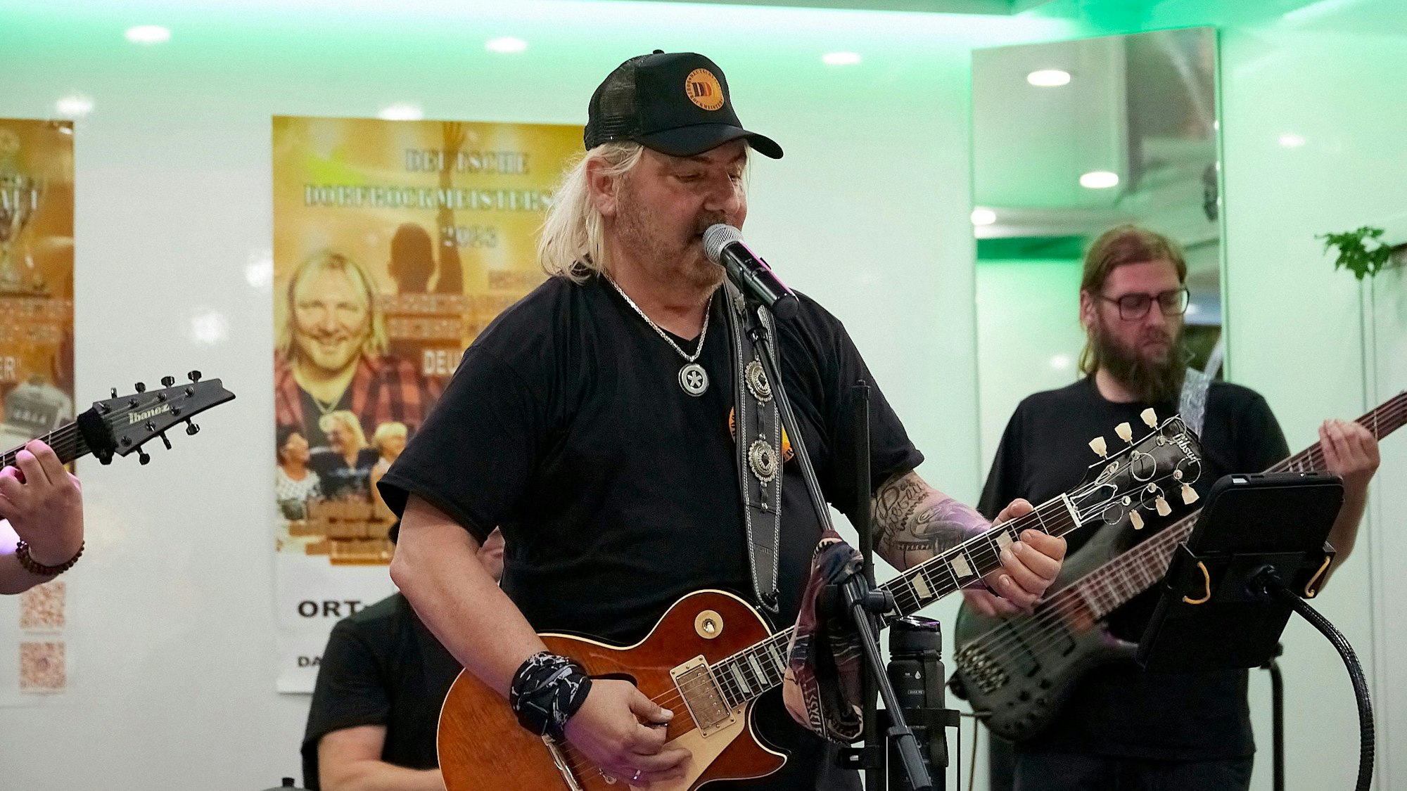 Der Musiker Remo Hopf singt in ein Mikrofon und spielt dazu E-Gitarre, im Hintergrund begleiten ihn weitere Musiker.