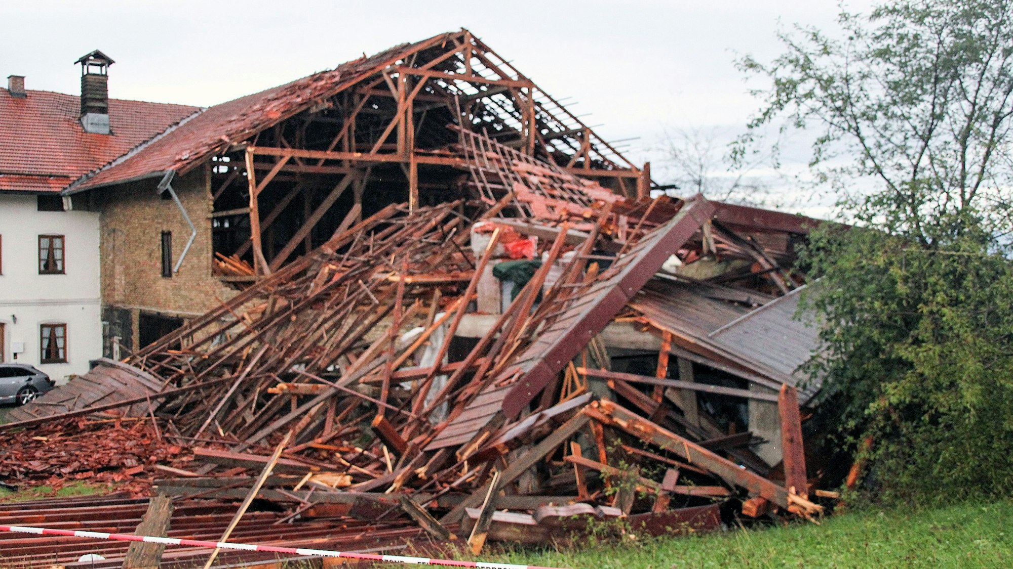 Holzbalken und Dachteile eines teilweise eingestürztes Hauses liegen nach einem heftigen Unwetter auf einem Grundstück.
