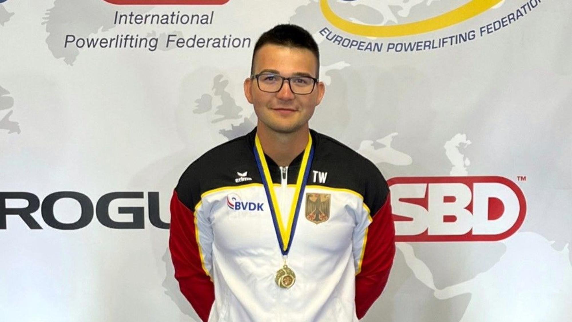 Ein Mann in Sportkleidung trägt eine Medaille um den Hals.