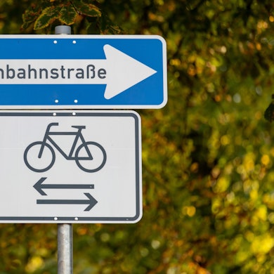 Das Bild zeigt ein Einbahnstraßen-Schild. Darunter: eine Abbildung eines Fahrrads. Pfeile zeigen in beide Richtungen.