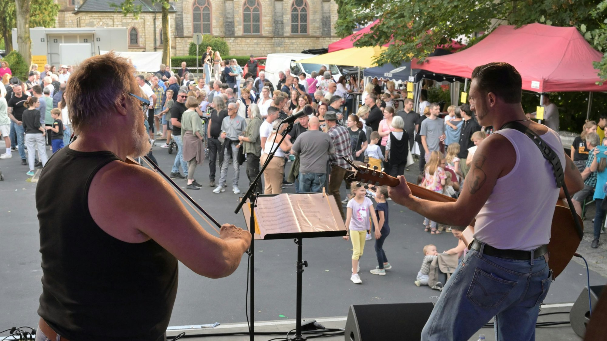 Zwei Musiker stehen auf der Bühne, im Hintergrund ist das Publikum zu sehen.