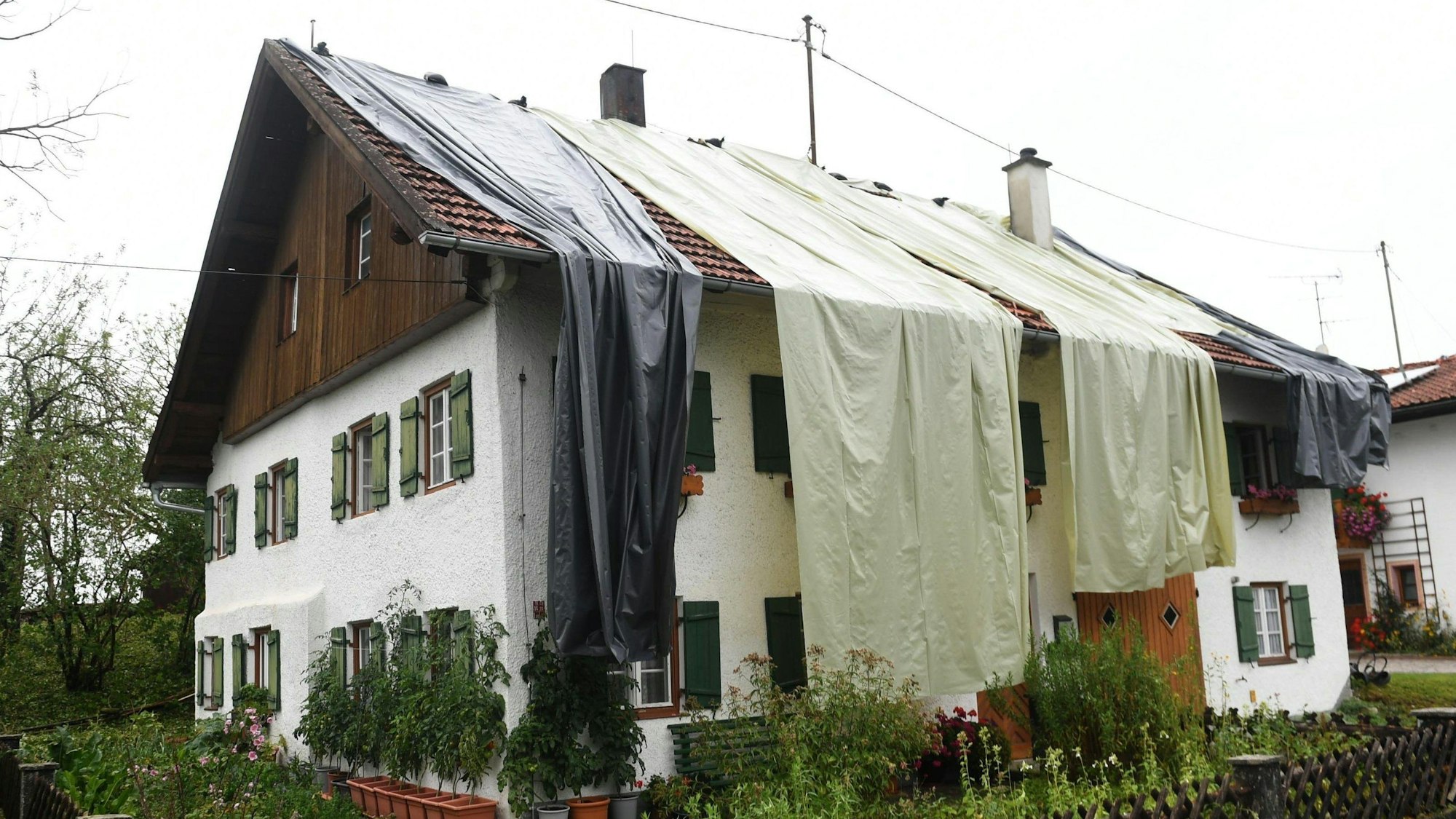 27.08.2023, Bayern, Bad Bayersoien: Nach dem Unwetter im Landkreis Garmisch-Partenkirchen ist das Dach eines Wohnhauses mit Planen provisorisch abgedeckt. Aufgrund schwerer Unwetterschäden rief das Landratsamt Garmisch-Partenkirchen für den Ort mit rund 1300 Einwohnern am Sonntag den Katastrophenfall aus. 80 Prozent der Gebäude in dem Ort sollen schwer beschädigt sein. Foto: Felix Hörhager/dpa +++ dpa-Bildfunk +++