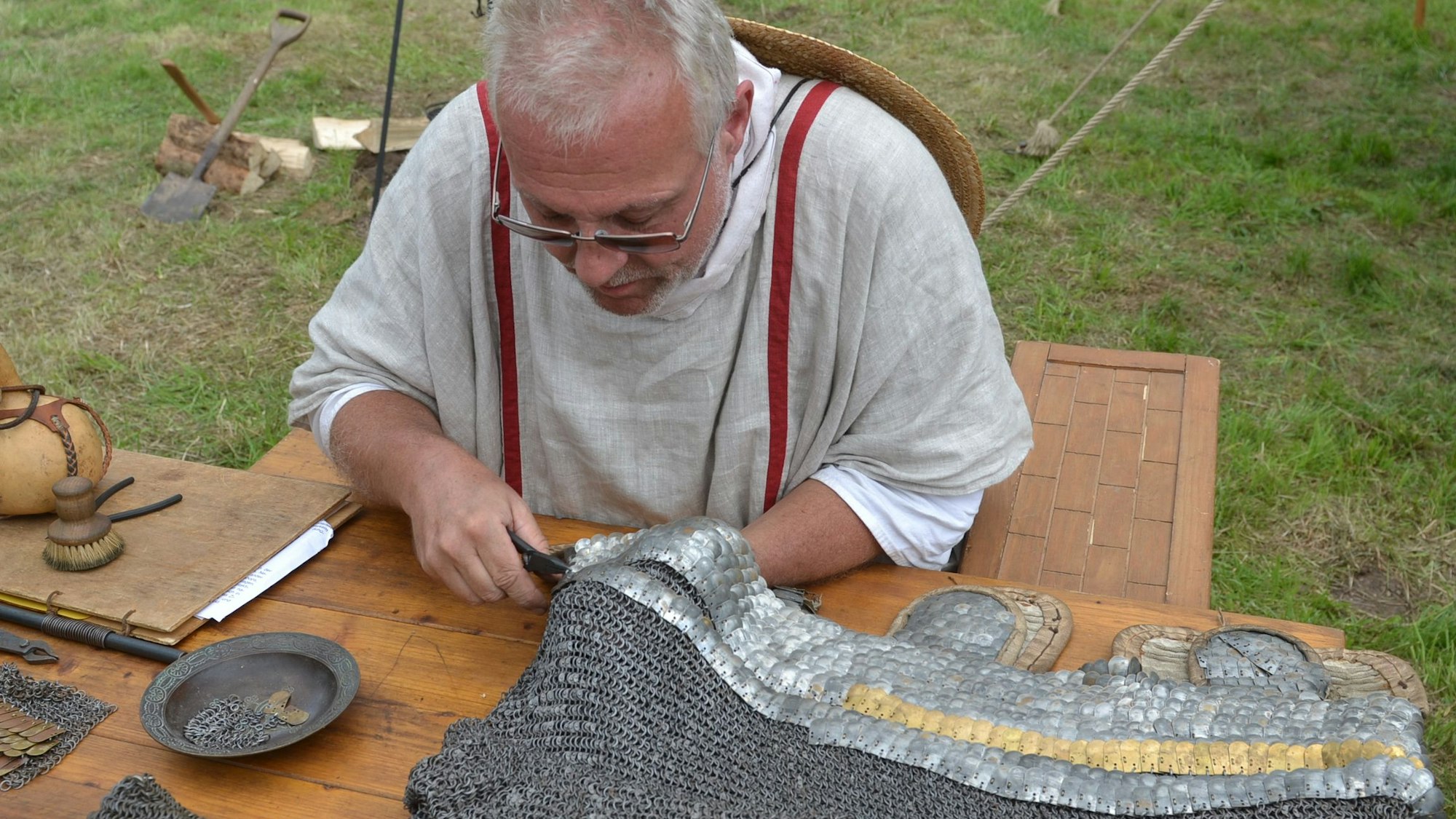 Ein Handwerker im mittelalterlichen Gewand arbeitet beim Mittelalterfest an einem Kettenhemd.