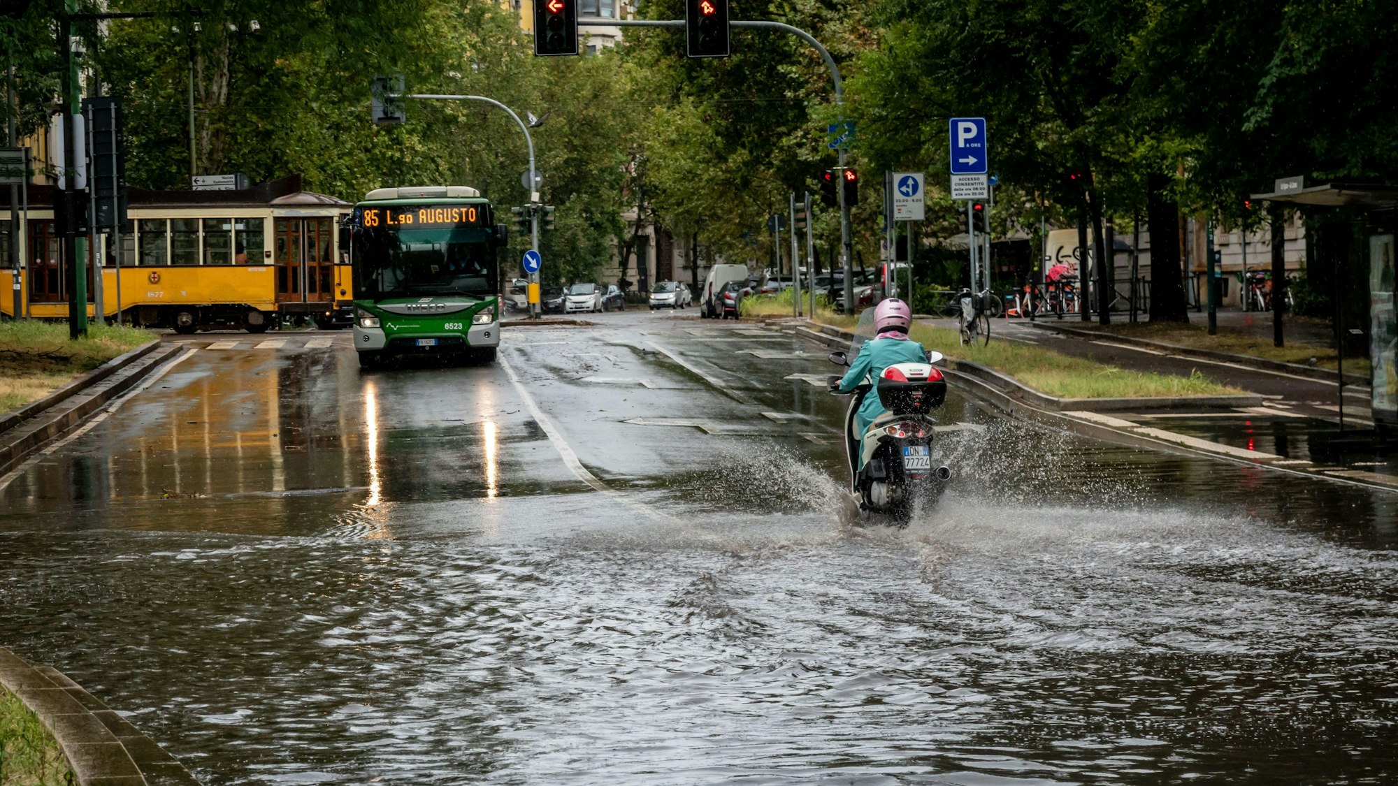 Eine Person fährt mit einem Motorroller eine überschwemmte Straße entlang.