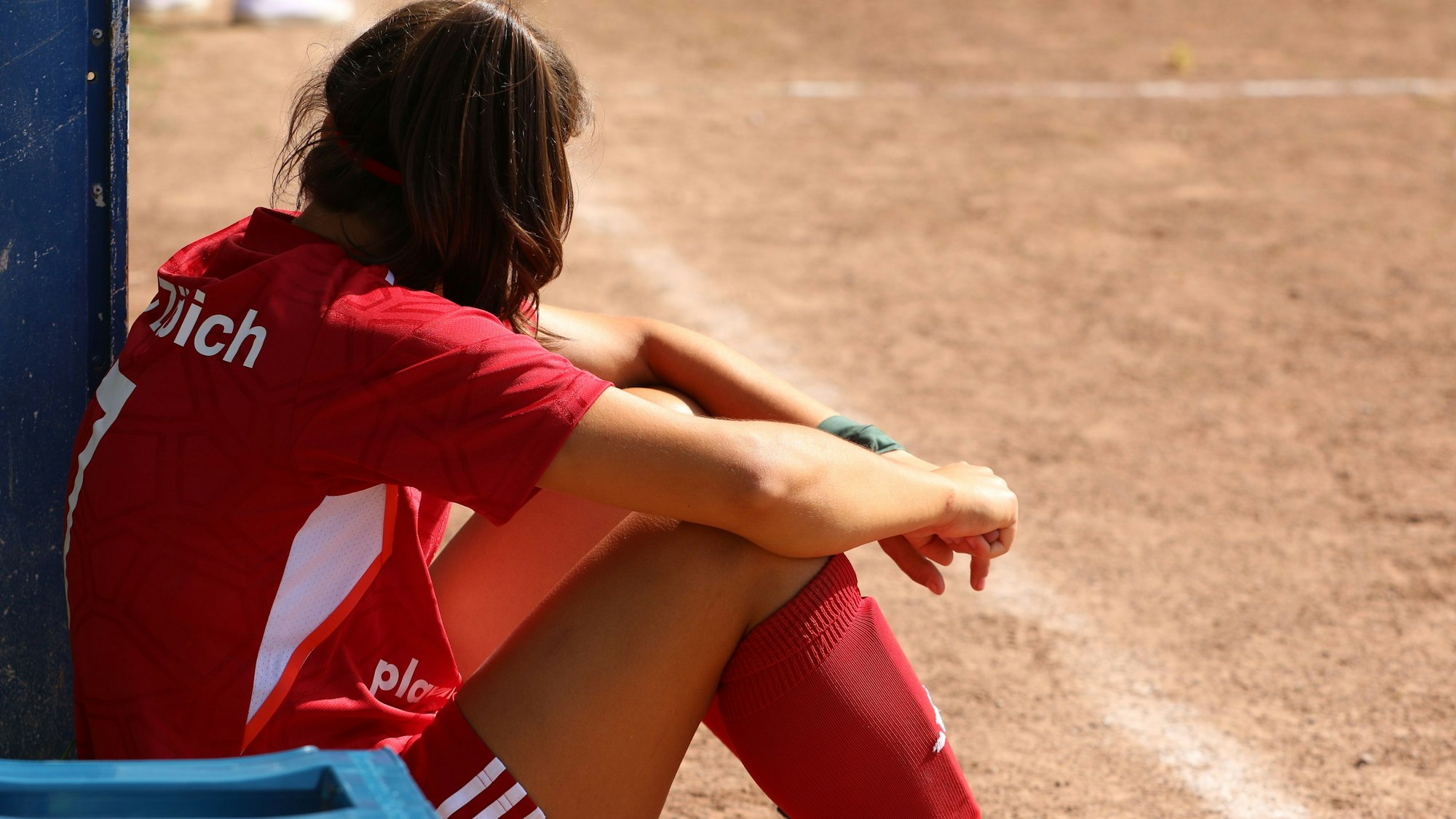 Eine des Feldes verwiesene Spielerin sitzt am Rand eines Aschenplatzes.