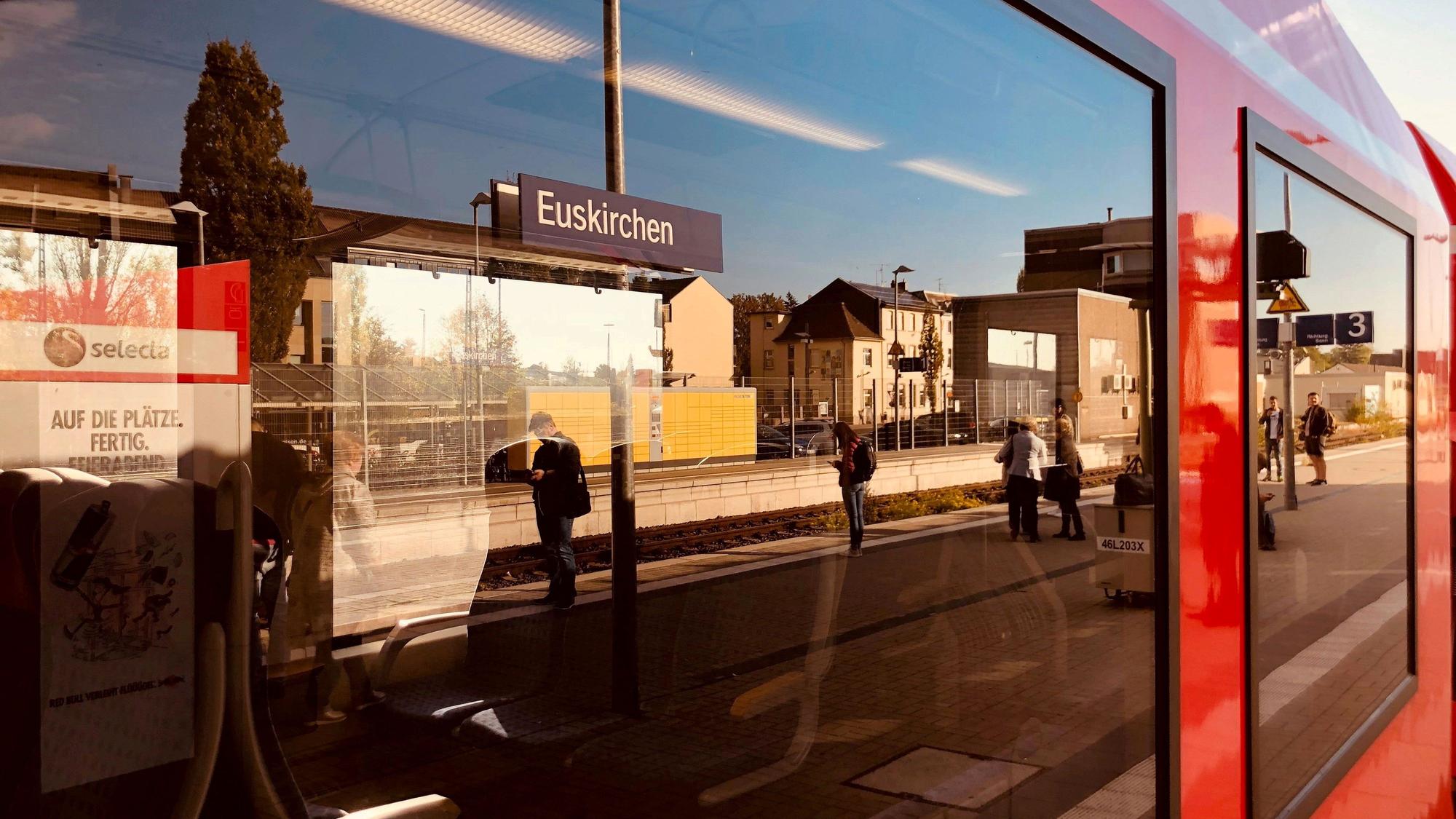 In der Fensterscheibe eines Waggons spiegelt sich ein Bahnsteig des Euskirchener Bahnhofs mit Reisenden, die auf einen Zug warten.