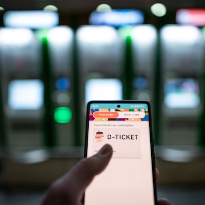 Ein Mann hält ein Mobiltelefon, auf dem das „D-Ticket“ gekauft werden kann, vor dem Ticketautomaten am Hauptbahnhof Essen in der Hand.